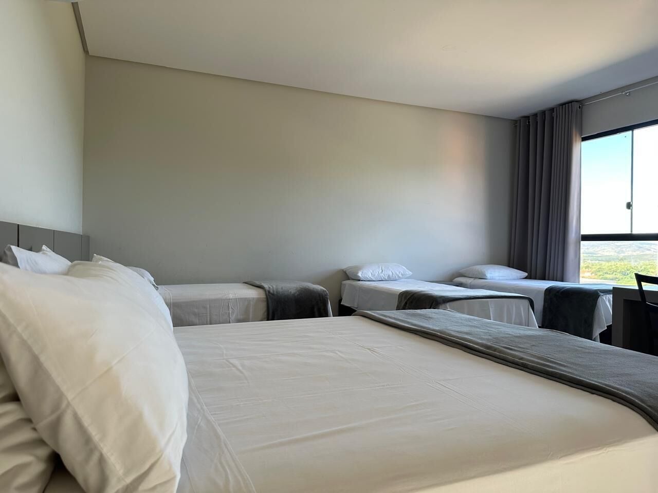 A hotel room with a large bed, two smaller beds, a desk, and a chair.