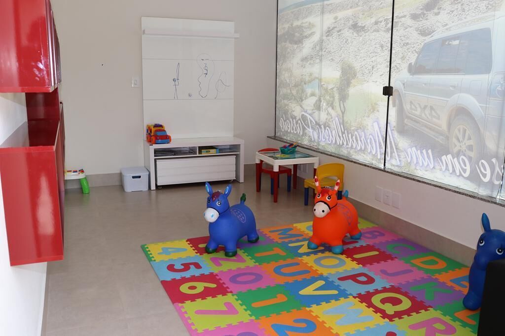 Un área de juegos infantiles con alfombras de espuma con el alfabeto, dos caballos de juguete y una pizarra con dibujos.