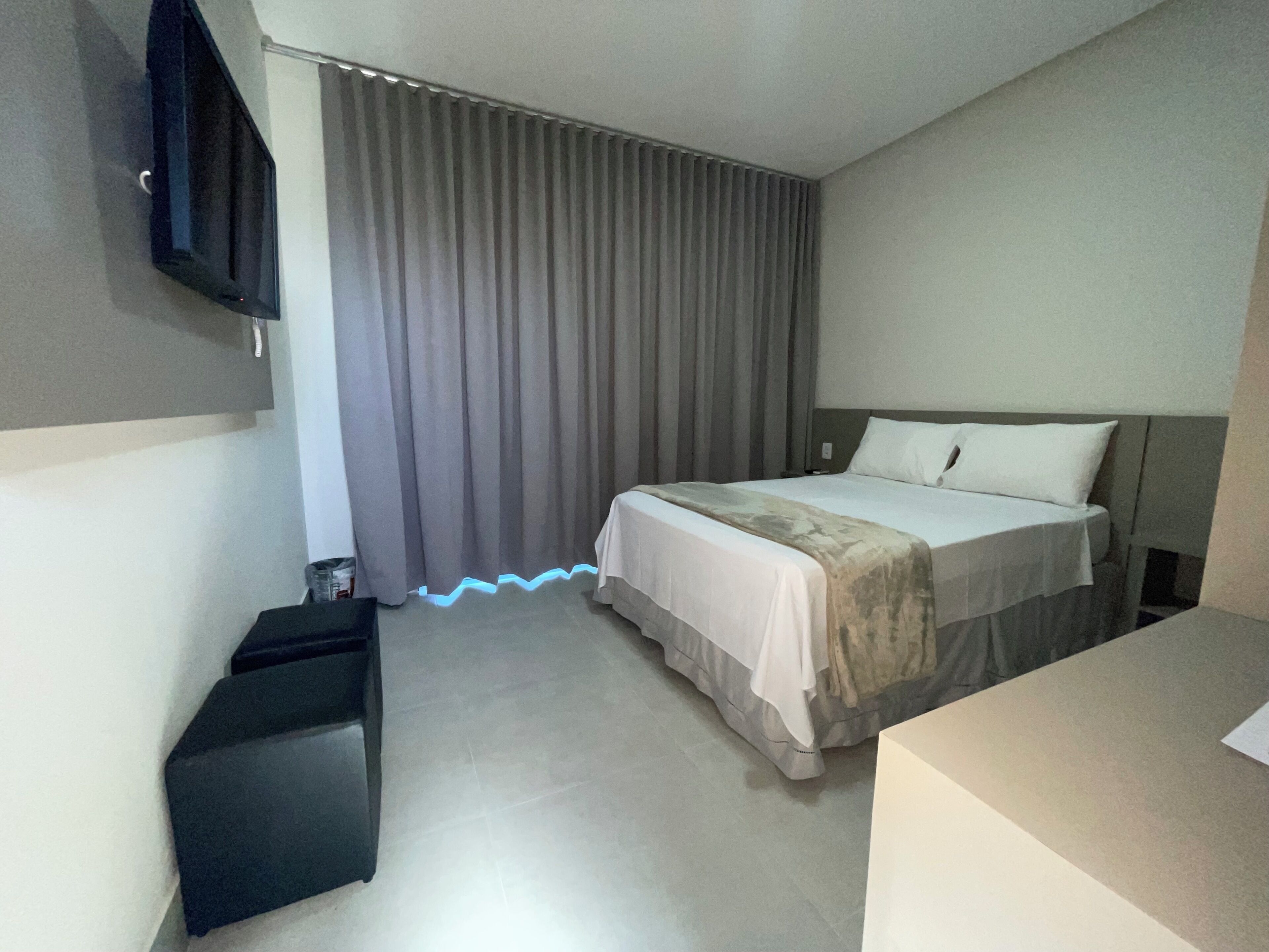 A hotel room with a bed, a TV mounted on the wall, a desk, and a chair.