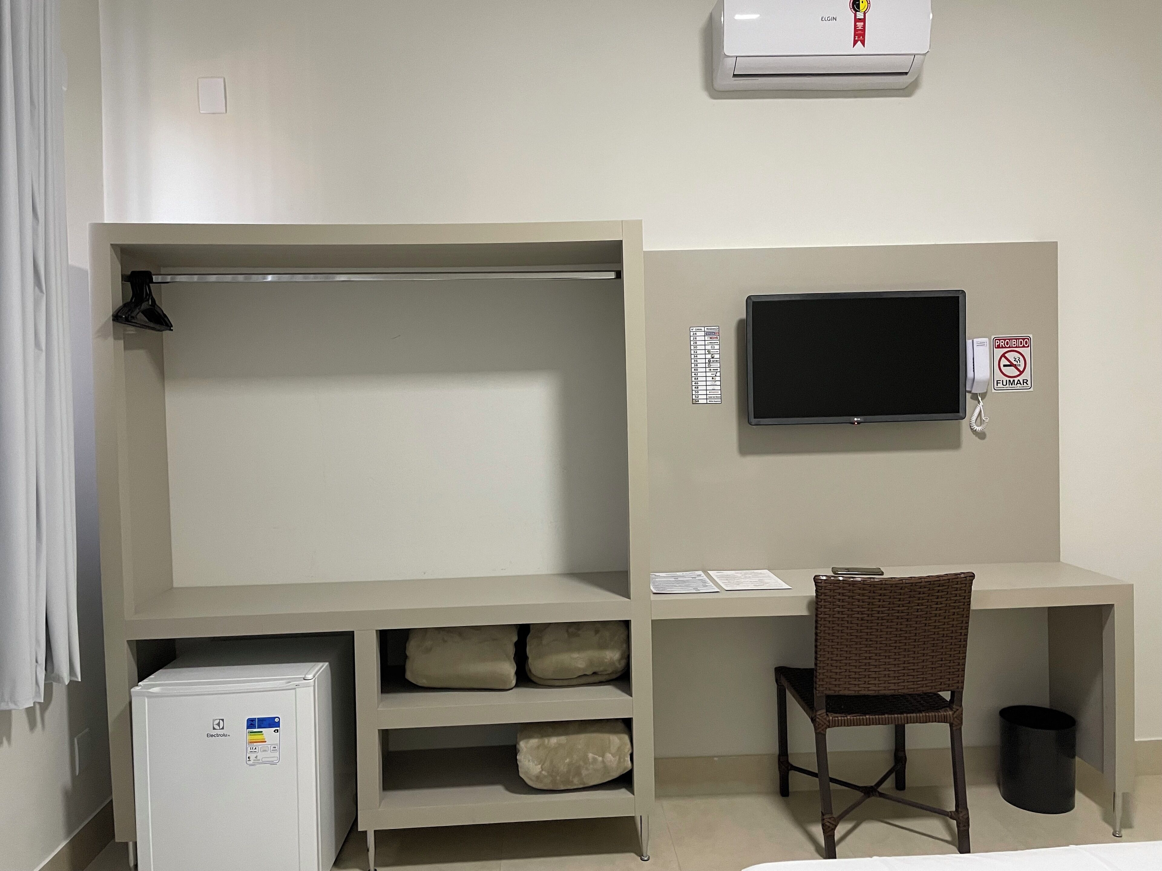 A room with a bed, a desk with a chair, a television, a refrigerator, and a wardrobe.