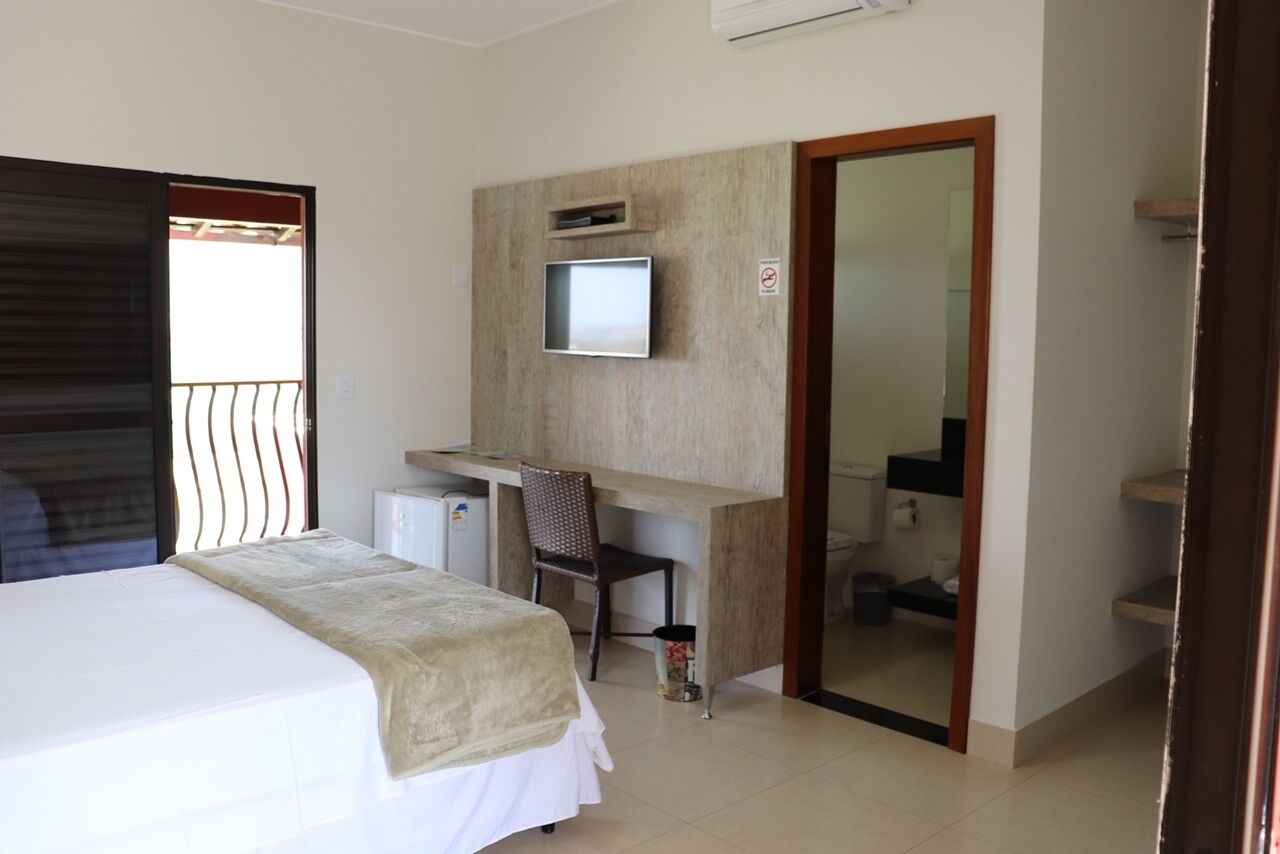 A hotel room with a bed, a desk, a chair, a television, and a bathroom visible through an open door.