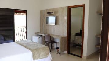 A hotel room with a bed, a desk, a chair, a television, and a bathroom visible through an open door.