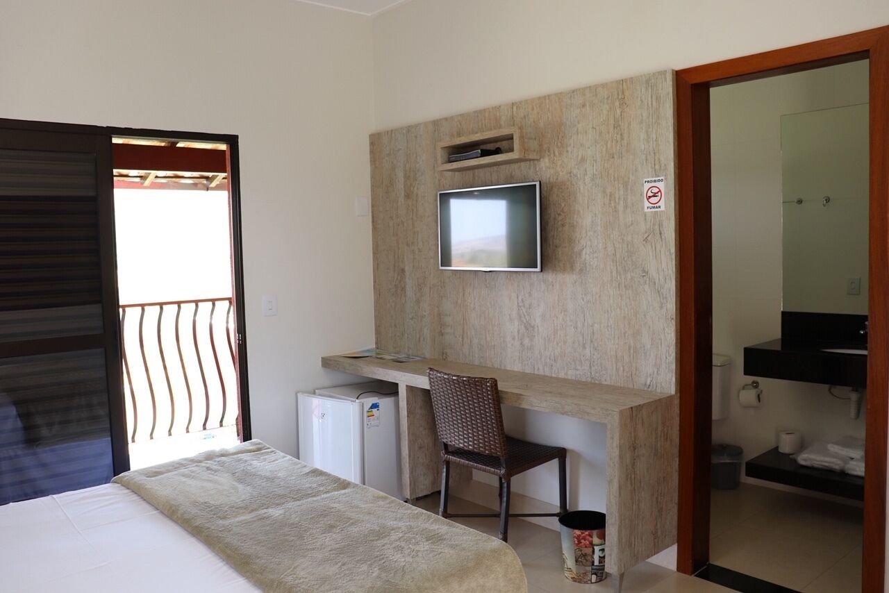 Habitación de hotel con cama, escritorio con televisor, refrigerador pequeño, una silla y baño visible a través de una puerta abierta.