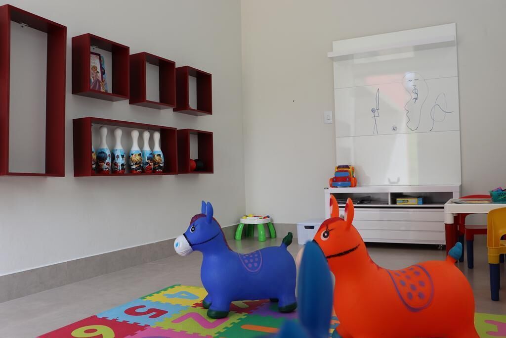 Een kinderspeelkamer met een kleurrijke speelmat, twee speelpaarden, een wit kastje en een muur met een ingelijste tekening.