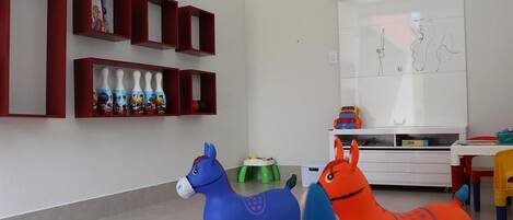 Un cuarto de juegos infantil con un tapete de colores, dos caballos de juguete, un armario blanco y una pared con un dibujo enmarcado.