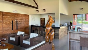 Een receptiezone met rieten meubels, een houten sculptuur en een klok aan de muur.