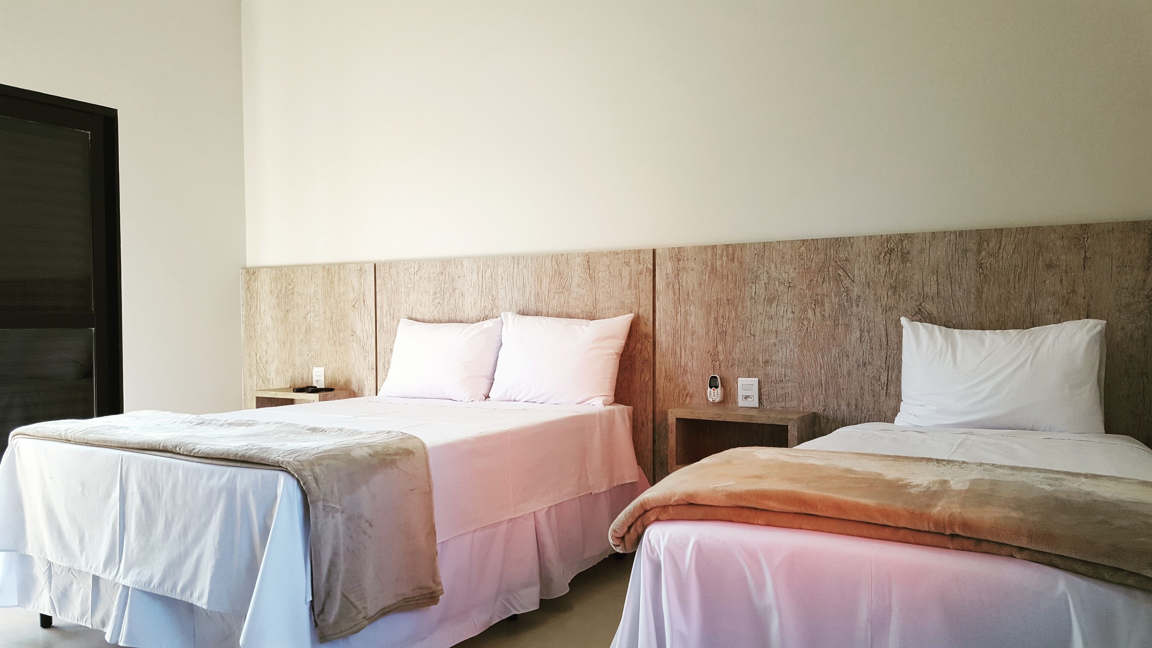 Une chambre d’hôtel avec deux lits, une tête de lit en bois, des tables de chevet et un téléphone fixé au mur.