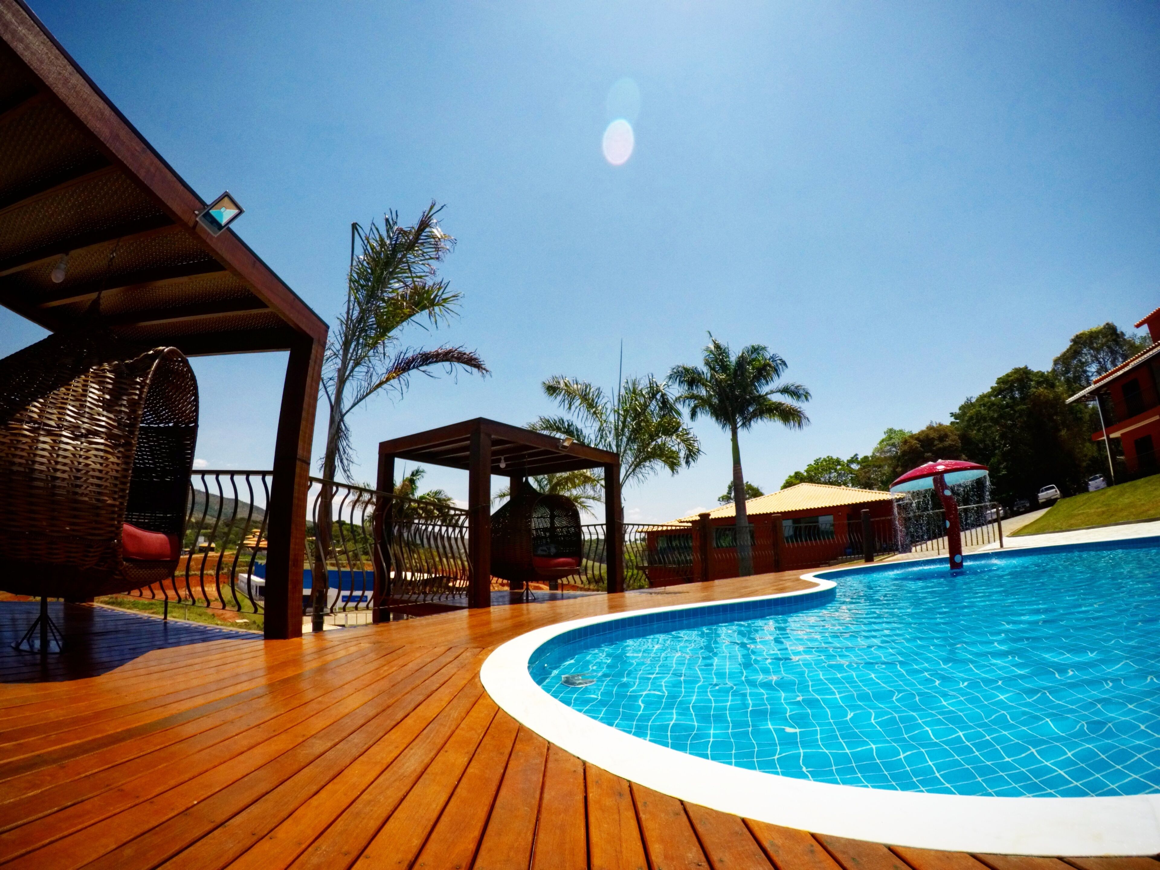 A wooden deck surrounding a swimming pool with palm trees and a gazebo.