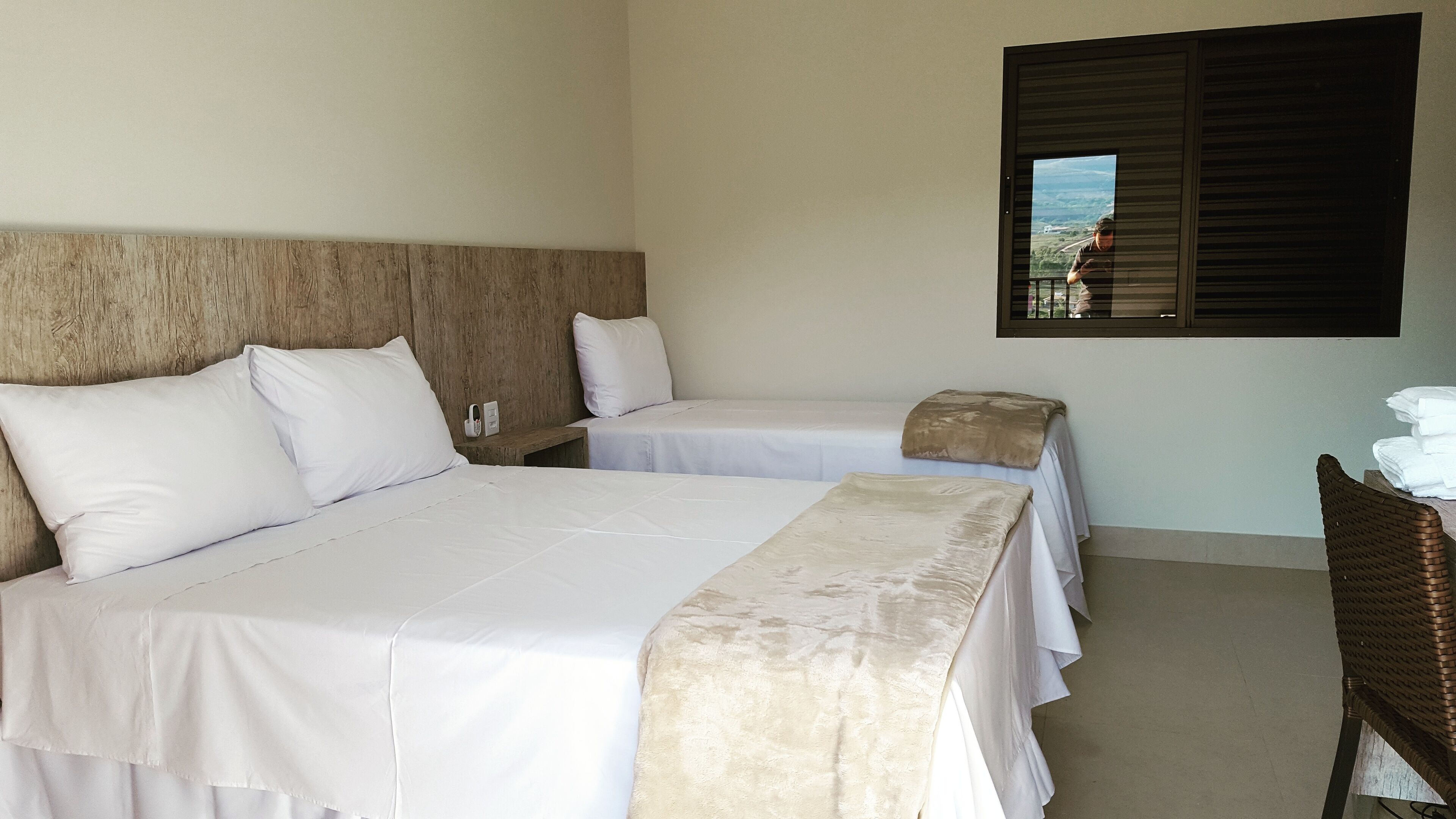A hotel room with two single beds, a wooden headboard, a small table, and a window with a view.