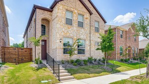 A two-story stone building with a brown roof, a front entrance, and a small front yard with a wooden fence and young trees. - 8 Mi to Celebration Station: Family Getaway! (Mesquite)