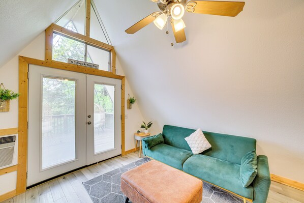 Una habitación acogedora con un sofá verde, un ventilador de techo de madera y un ventanal grande.