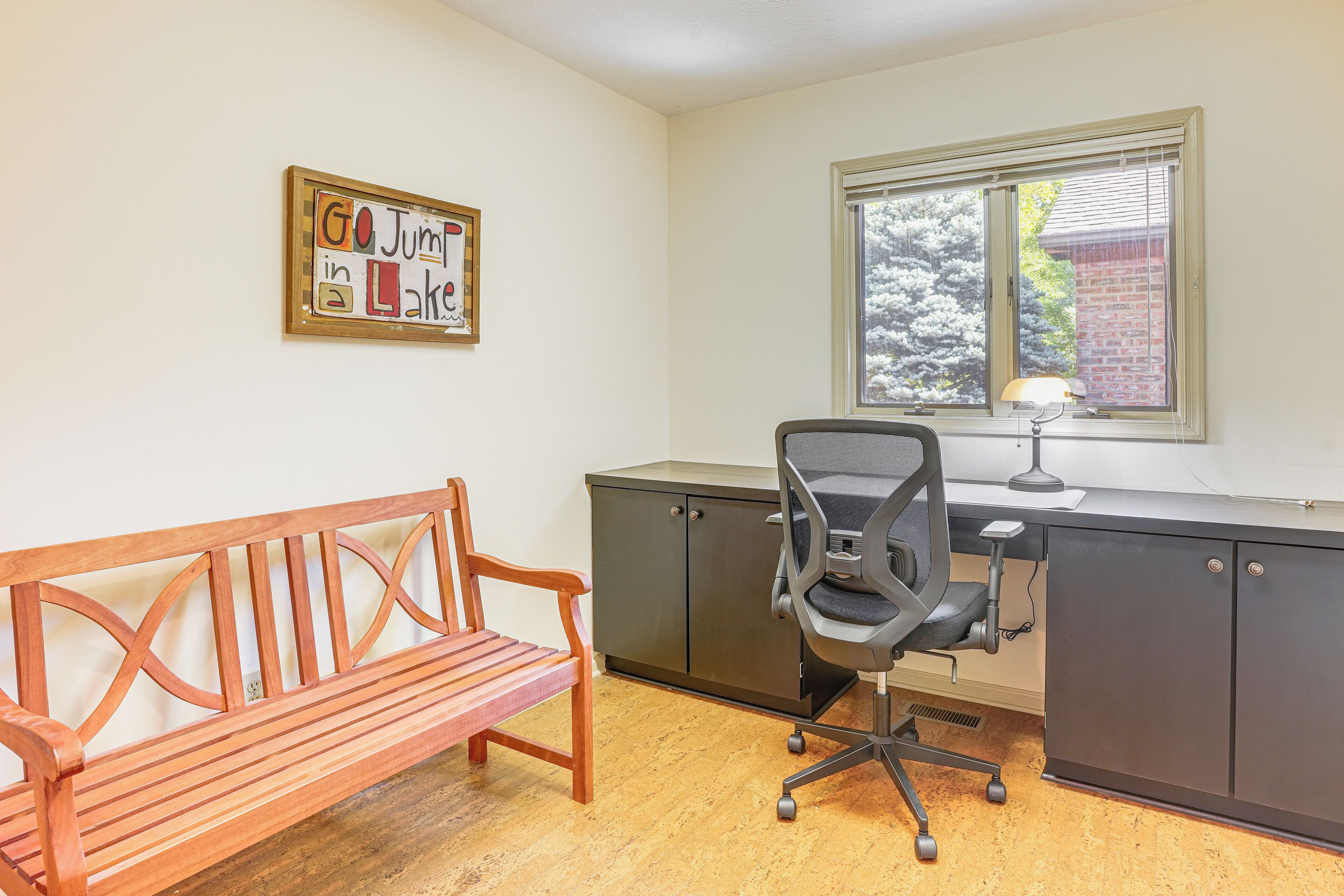 A room with a wooden bench, a desk with a chair, and a window with blinds.
