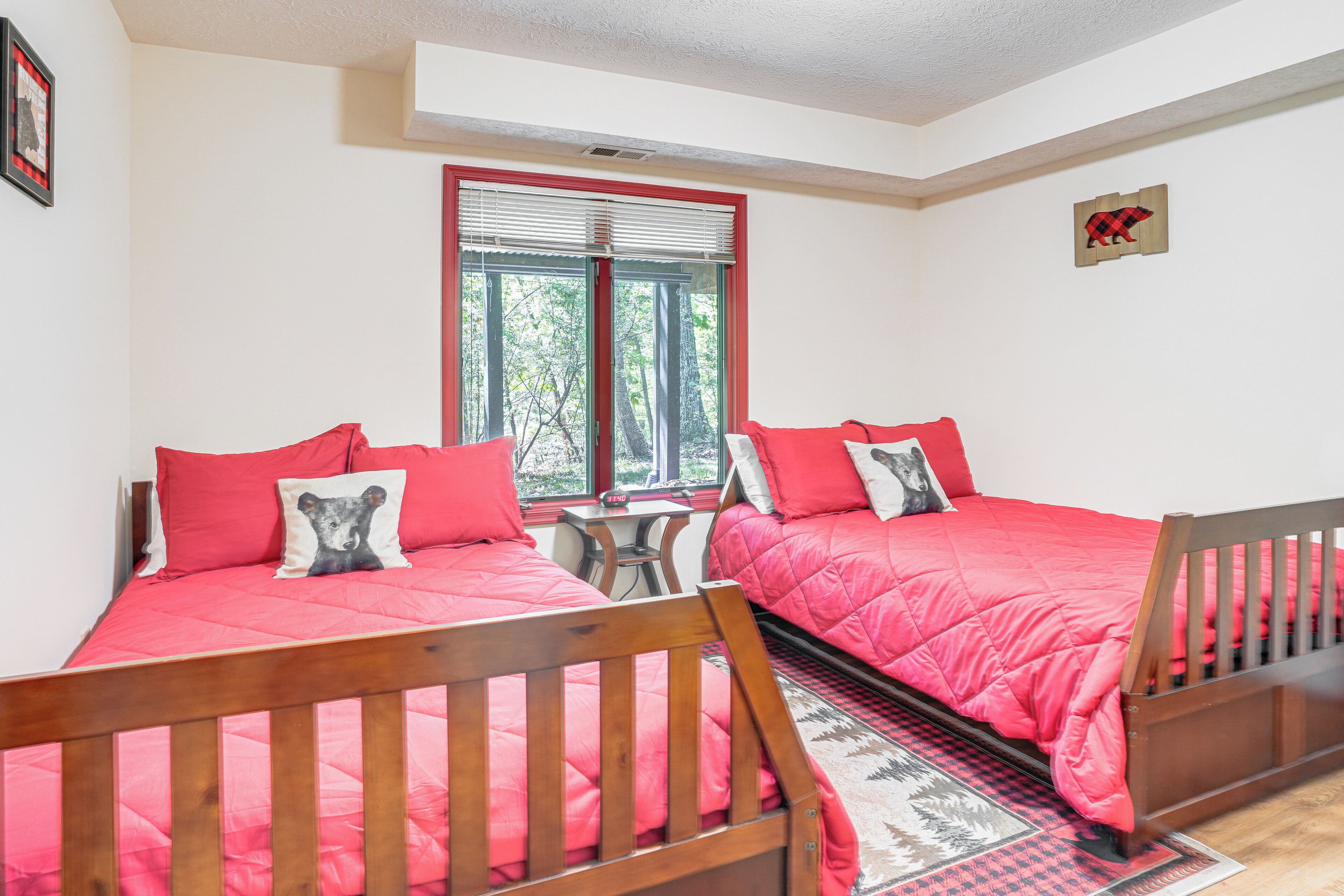 A bedroom with two beds, each with a red bedspread and matching pillows, a small table, and a window with blinds.