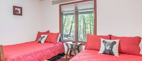 Una habitación con dos camas, cada una con ropa de cama y almohadas rojas, una mesita de madera y un ventanal con persianas.
