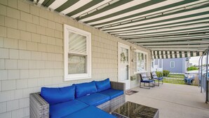 A covered patio area with a blue sofa, wicker chairs, and a glass-top coffee table.