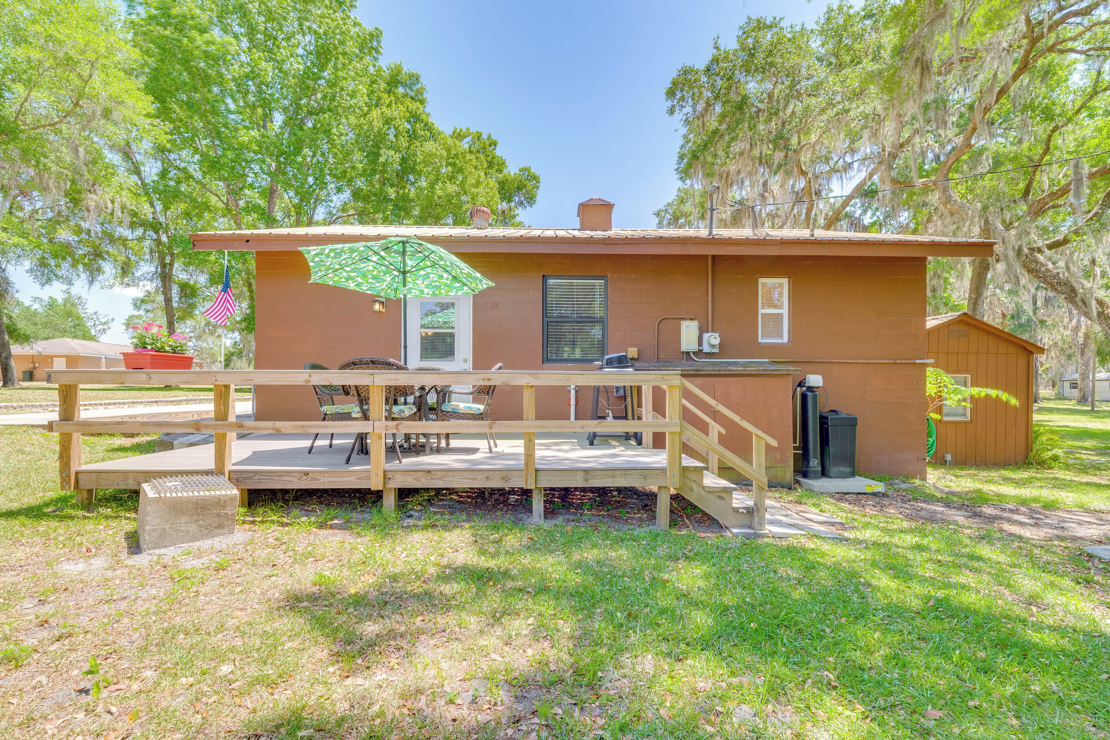 A small, single-story cabin with a wooden deck, a patio table, and an American flag.