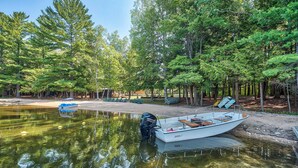 A serene lakeside setting with a boat docked on the shore, surrounded by lush greenery and trees. - Beach + Game Room Access: Lakefront Levering Cabin (Levering)