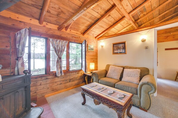 A cozy cabin interior with wooden walls, a sofa, a table, and a fireplace. - Lakefront Cabin w/ Beach Access: Levering Retreat (Levering)