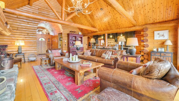 Een vakantiehuisje van binnen, met een hoge plafond, houten wanden, een open haard, lederen meubels en een kroonluchter.