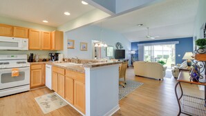 A spacious kitchen with wooden cabinets, a central island, and a dining area with a chair and table. - Walk to Community Perks: Home in The Villages (The Villages)