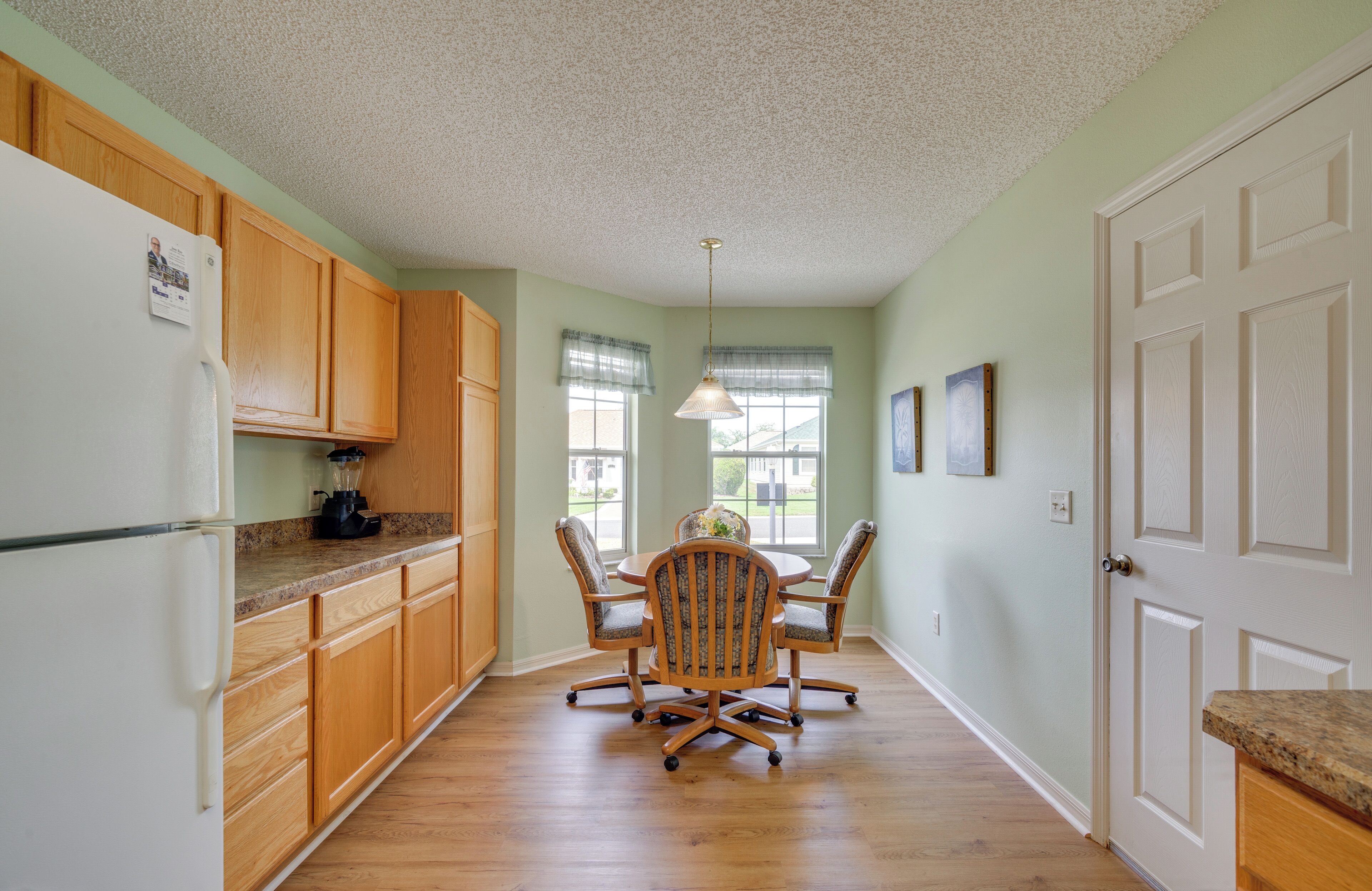 A kitchen with wooden cabinets, a refrigerator, a dining table with chairs, and a pendant light.