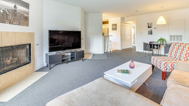 Ein modernes Wohnzimmer mit Flachbildfernseher, Kamin, Essbereich mit Tisch und Stühlen sowie einem farbenfrohen, gemusterten Sofa.