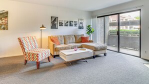 Ein modernes Wohnzimmer mit Sofa, Sessel und Couchtisch, einem großen Fenster mit Aussicht und Wandbildern.