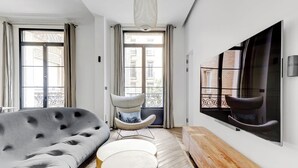 A modern living room with a grey sofa, a round blue coffee table, a wooden bench, and a large TV mounted on the wall. - Luxury Apt - 4P/2BDR - Arc de Triomphe (Paris)