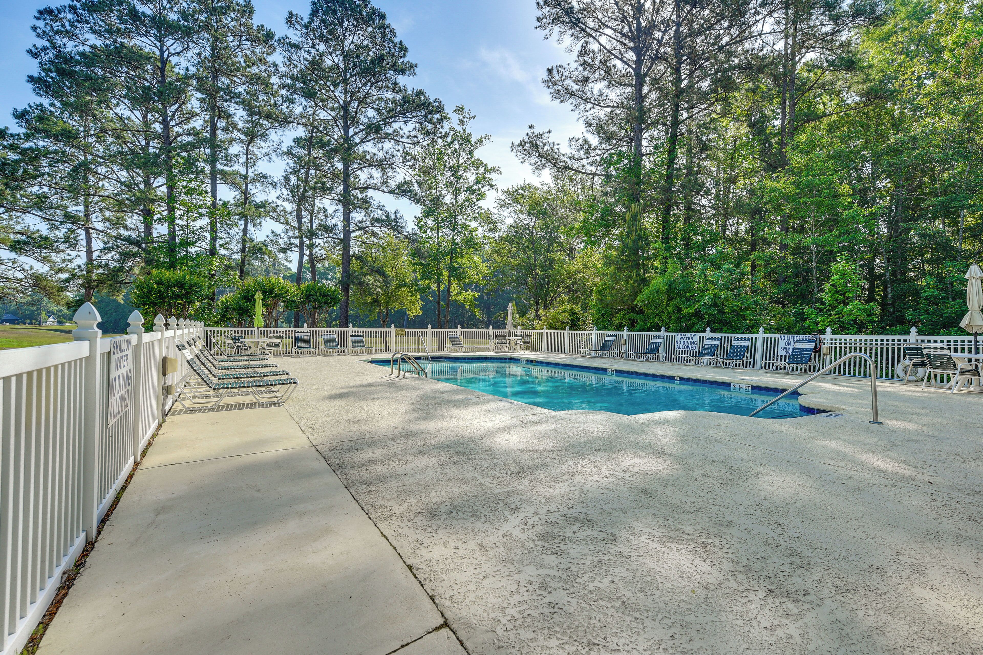 A swimming pool surrounded by a white fence, with trees in the background.