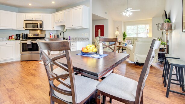 A modern kitchen with white cabinets, a stainless steel microwave, and a dining area with a wooden table and chairs. - Deck & Yard: Savannah Area Retreat! (Pooler)