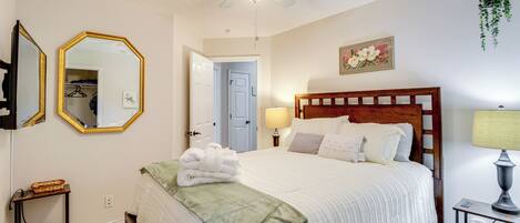 A neatly arranged bedroom with a bed, bedside tables, a ceiling fan, a mirror, and a door leading to a closet.