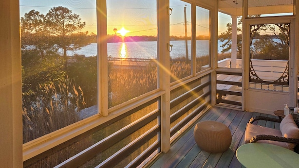 A covered porch with a view of the sunset over water, wooden railings, and outdoor seating. - Hot Tub & Bay Views: Outer Banks Home (Kill Devil Hills)