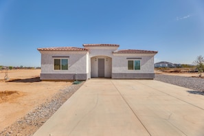 Stucco house with a central entrance and two small windows, set amidst a natural landscape.