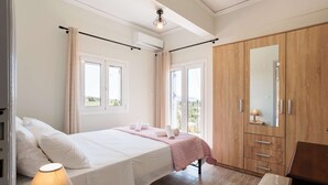 A bedroom with a bed, a chair, a wardrobe, and a window. - Seaview Serenity - Beachside Getaway (Trifylia)