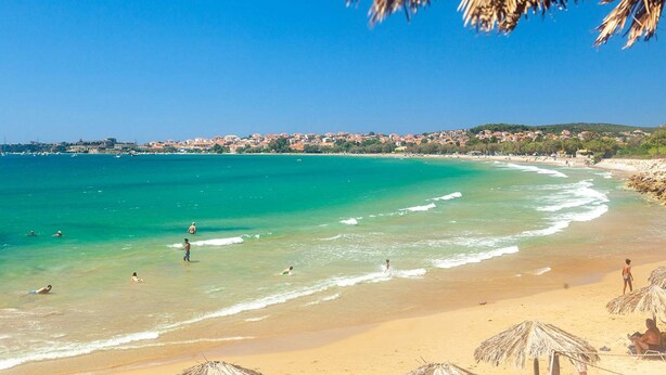 A beach with clear turquoise water, a sandy shore, and a distant town. - Seaview Serenity - Beachside Getaway (Trifylia)