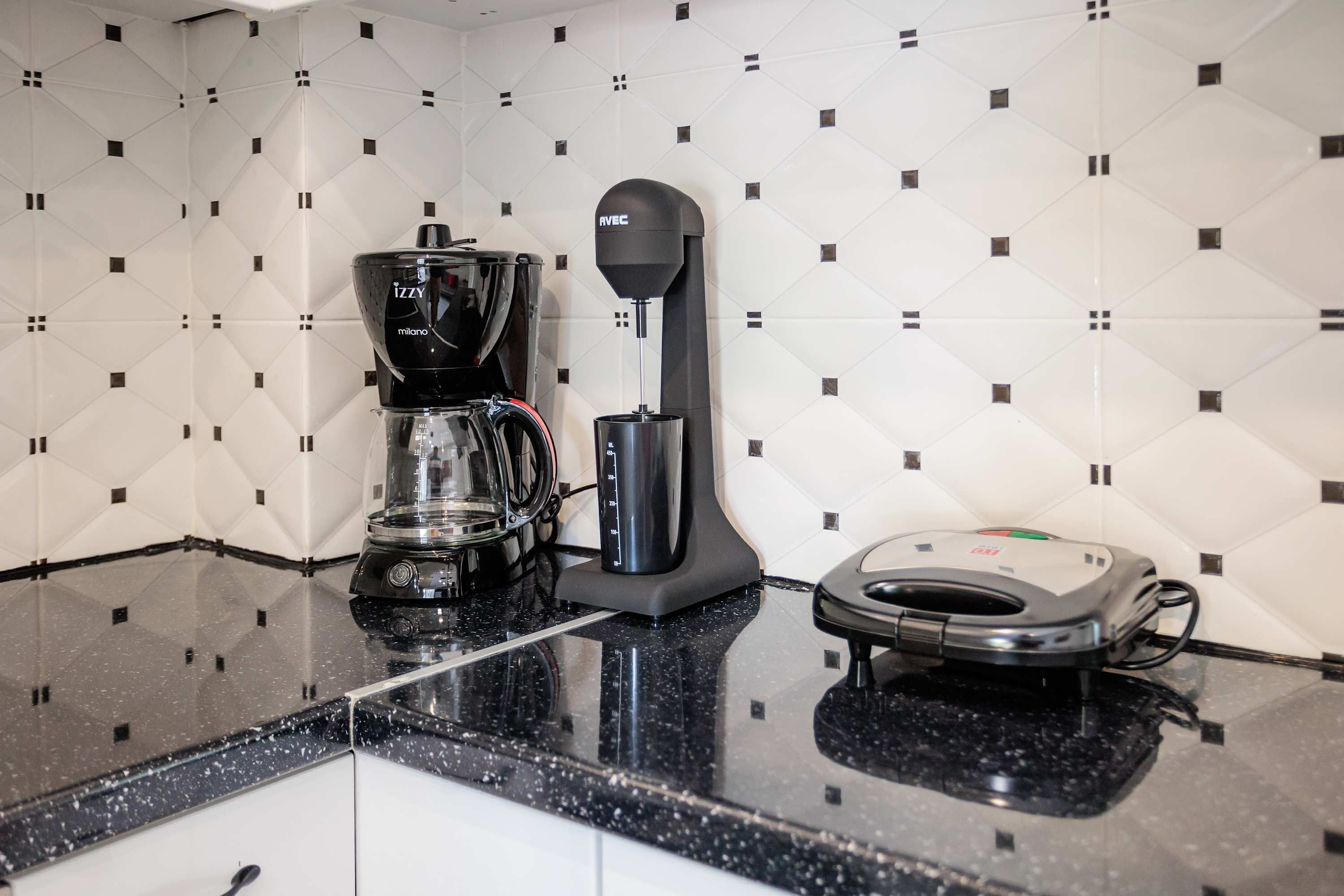 A kitchen with a coffee maker, a blender, and a vacuum cleaner on a black countertop.