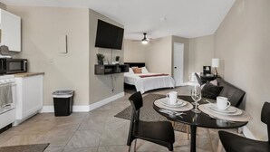 A modern hotel room with a dining area, kitchenette, and a bed with a TV.
