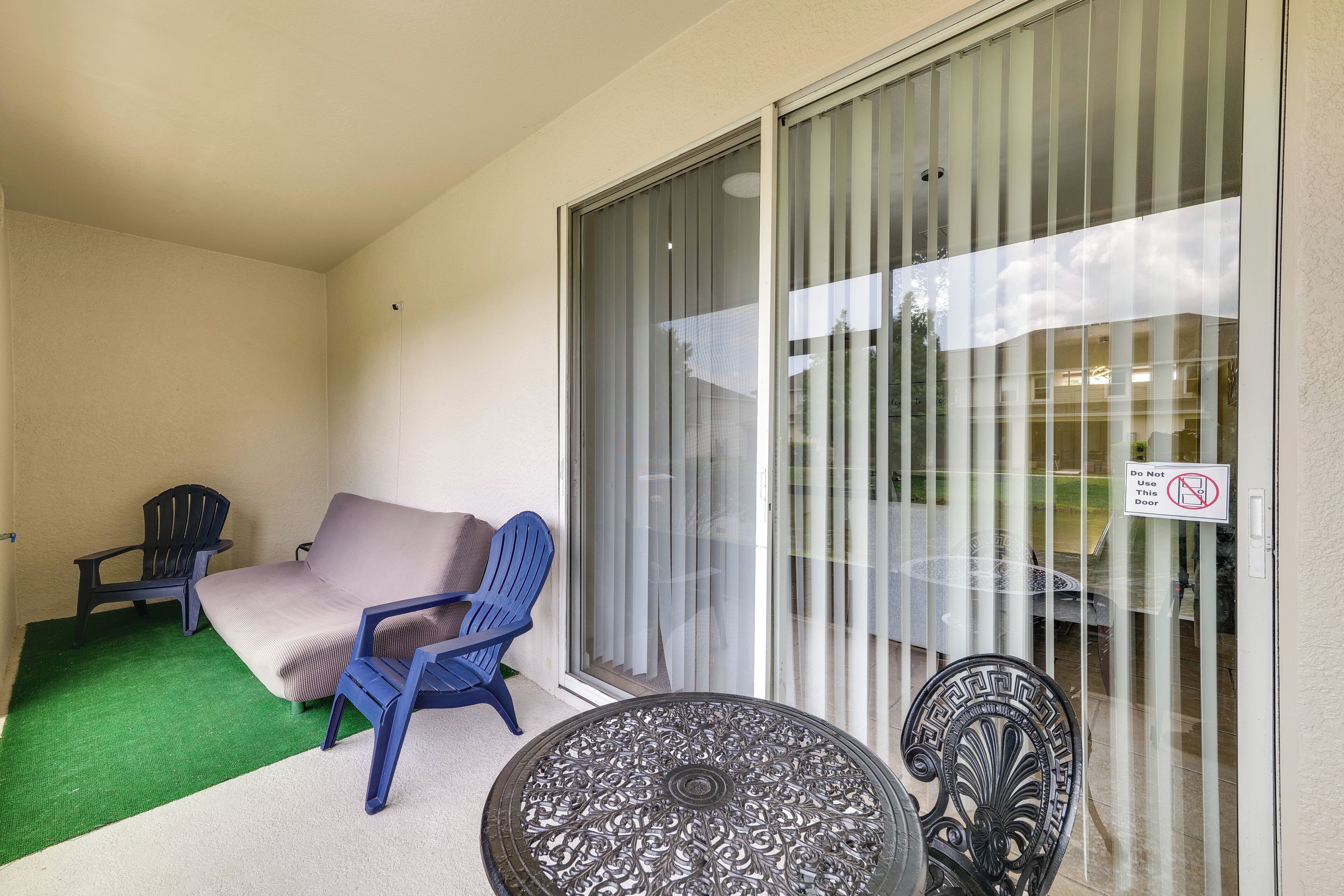 Un balcon avec un canapé, deux chaises, une table et une porte-fenêtre coulissante sur laquelle est apposée une pancarte indiquant : « Ne pas utiliser cette porte ».