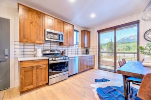 A modern kitchen with wooden cabinets, stainless steel appliances, and a large window offering a mountain view.