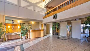 A spacious lobby with a reception desk, potted plants, and a high ceiling with natural light.