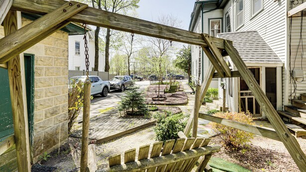A wooden swing set in a residential area with houses, parked cars, and a small garden. - Explore Dtwn, Parks & Colleges: Cozy Worcester Apt (Worcester)