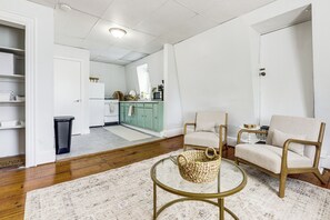 A living room with a round glass coffee table, two armchairs, a woven basket, and a kitchen in the background. - Explore Dtwn, Parks & Colleges: Cozy Worcester Apt (Worcester)