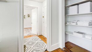 A hallway with white walls, a patterned rug, and a wooden floor. There are white storage boxes on shelves and a door leading to another room. - Explore Dtwn, Parks & Colleges: Cozy Worcester Apt (Worcester)