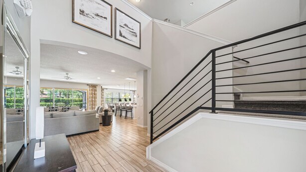 A spacious living area with a modern staircase, a dining area, and a view of greenery through large windows.