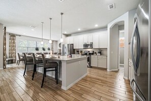 A modern kitchen with a central island, stainless steel appliances, and a dining area with chairs. - Spacious Home w/ Private Pool/Spa! *Sleeps 21* (Davenport)