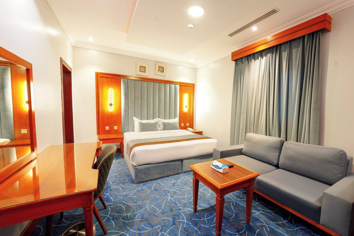 A hotel room with a bed, a sofa, a desk, and a mirror.