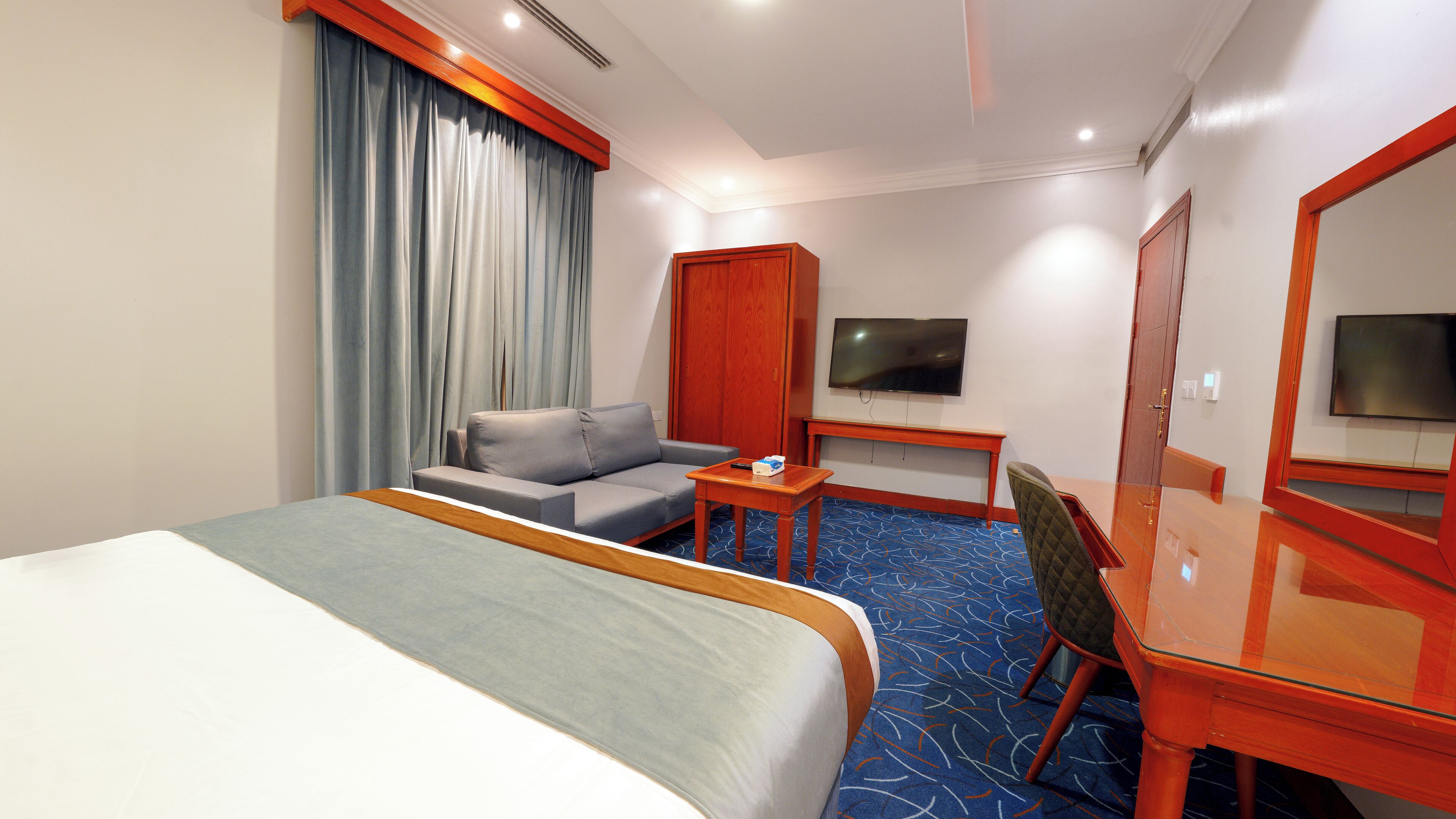 A hotel room with a bed, a sofa, a desk, a TV, and a wardrobe.