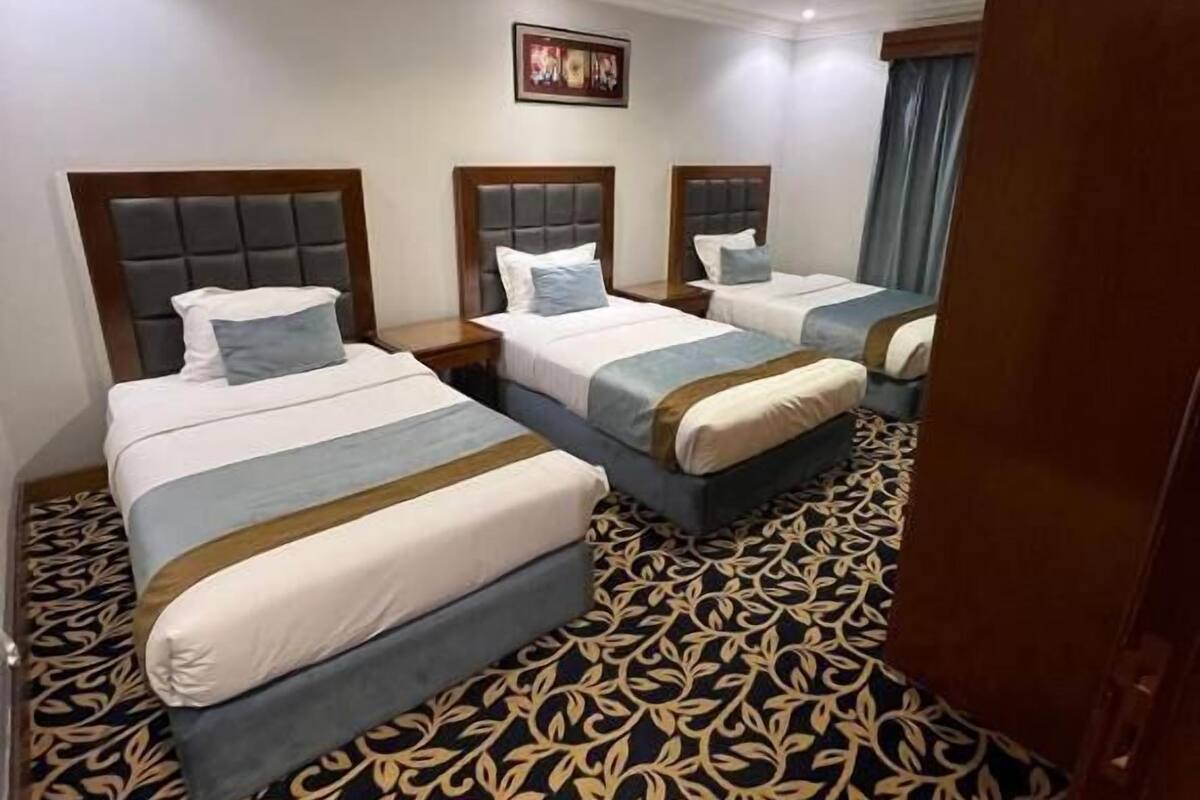 A hotel room with three beds, a patterned carpet, and a framed picture on the wall.