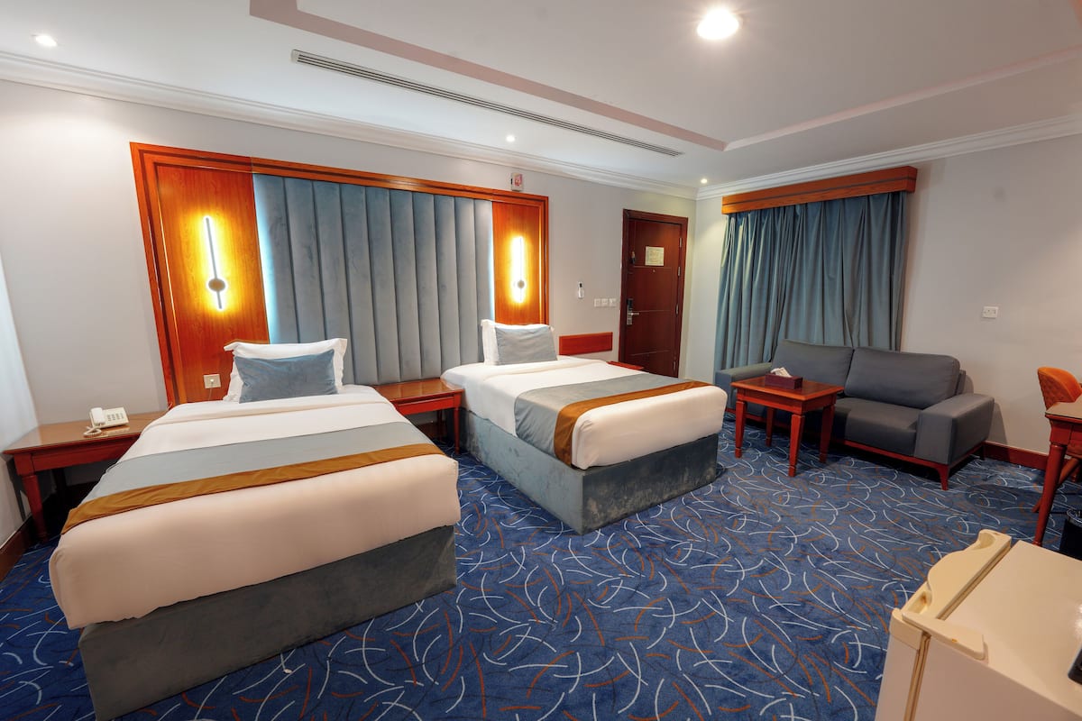 A hotel room with two beds, a sofa, a small table, and a desk.