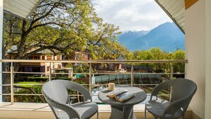 A balcony with wicker chairs and a table, overlooking a mountainous landscape and a garden. - Moustache Pahalgam (Anantnag)